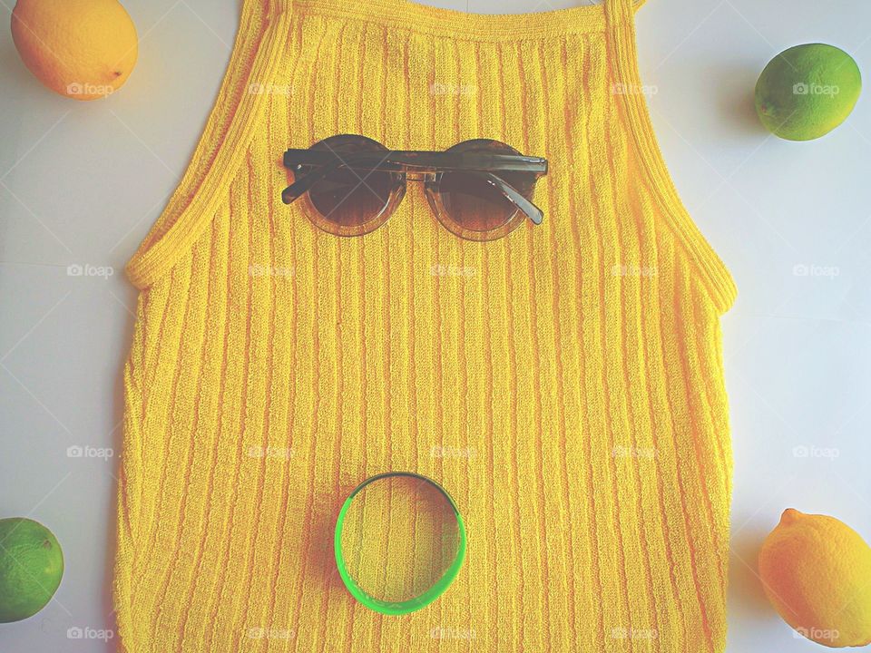 Yellow tank top with sunglasses, a bracelet, limes and lemons on a white background 