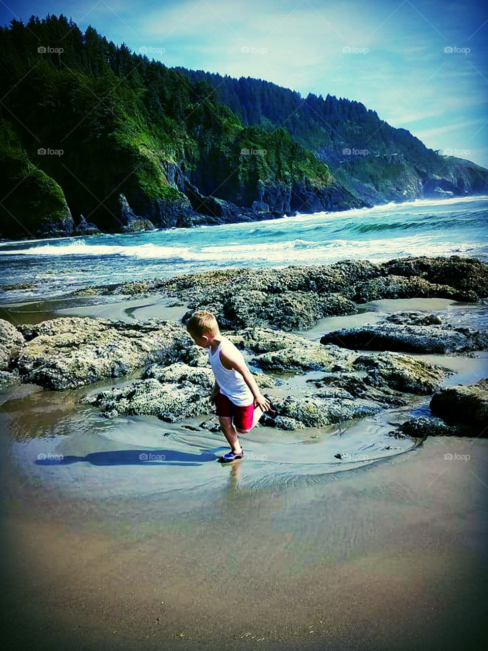 Boy frolicks carelessly, in glistening sand amidst the colorful Oregon coastline.