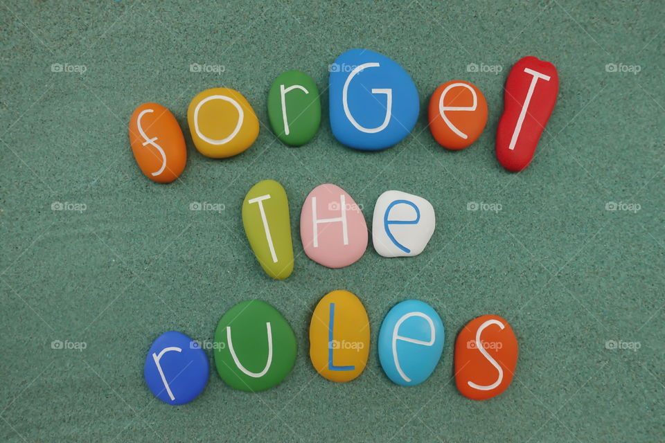 Forget the rules, motivational words composed with multi colored stones over green sand