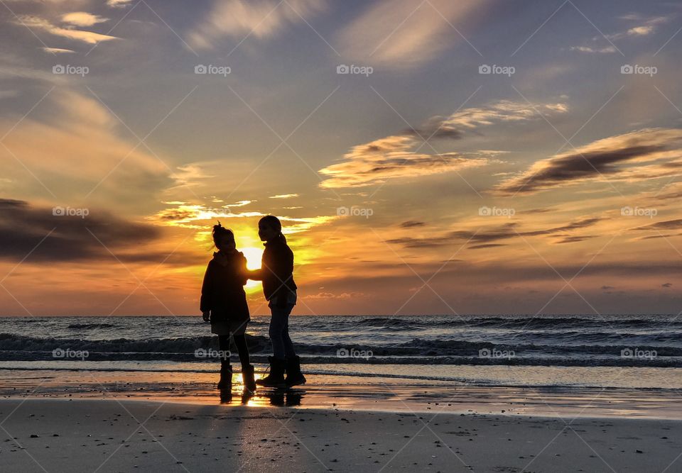 Two girls playing at the beach while the sun sets behind them. It was a cold day, but the girls loved it.