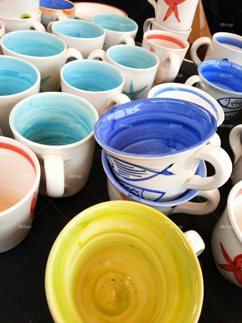 set of handmade ceramic objects made up of bowls and cups of various colors, displayed for sale