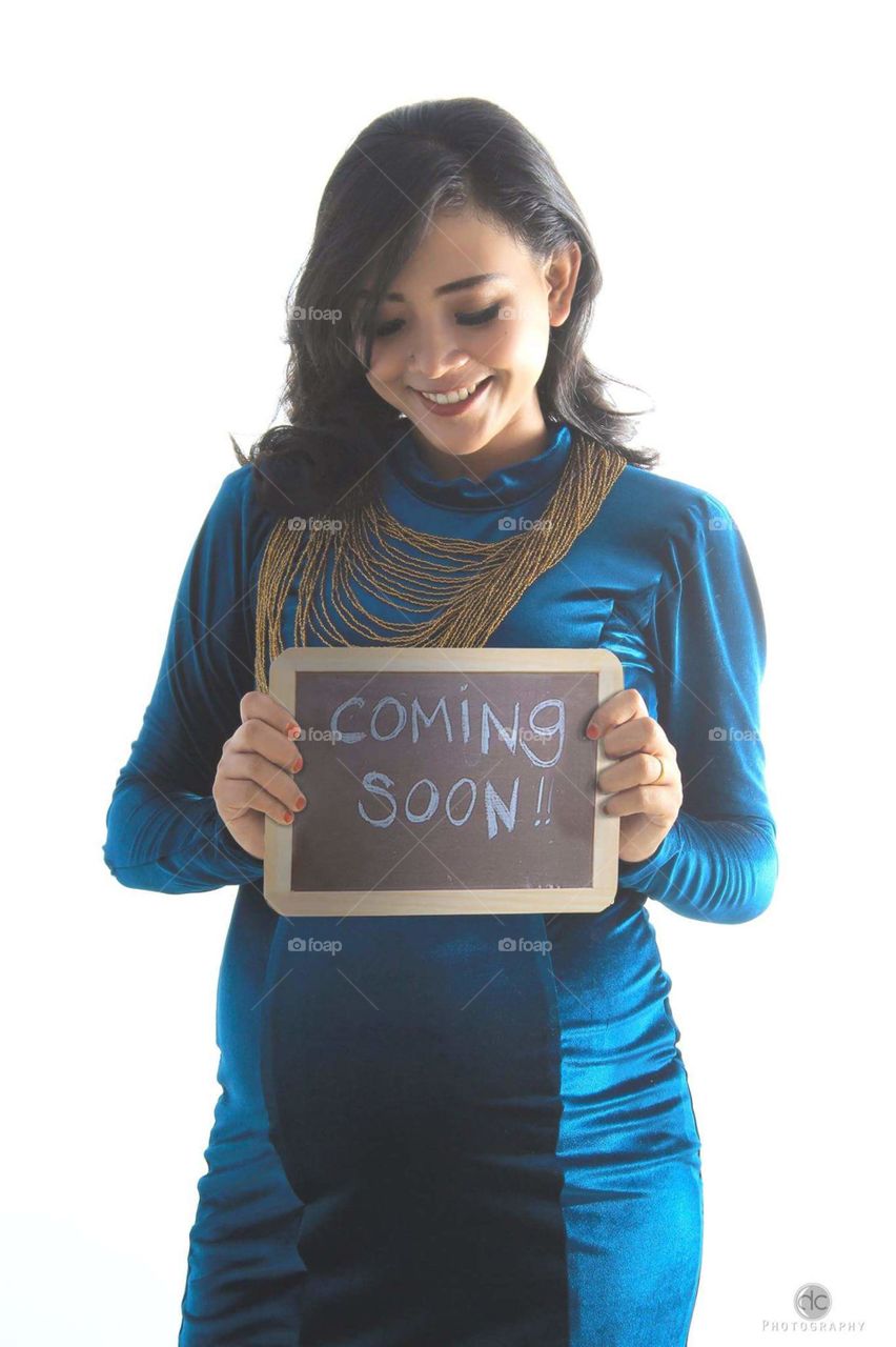 Pregnant woman holding slate with text of coming soon