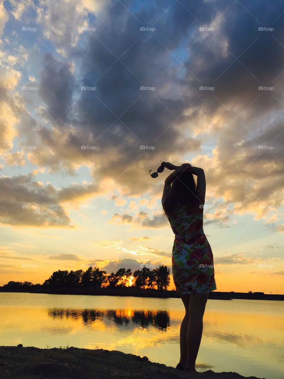 Rear view of woman posing near lake at sunset