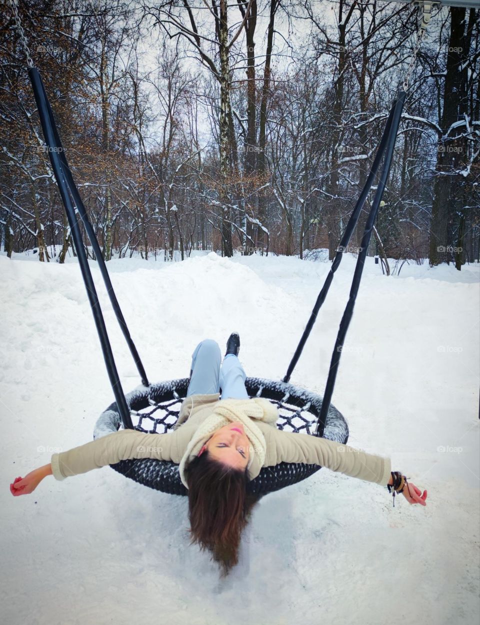 Winter.  Winter park in the snow.  A woman lies on a hanging swing with outstretched arms.  Feeling of flight, freedom and peace.  Cold beauty of nature in winter