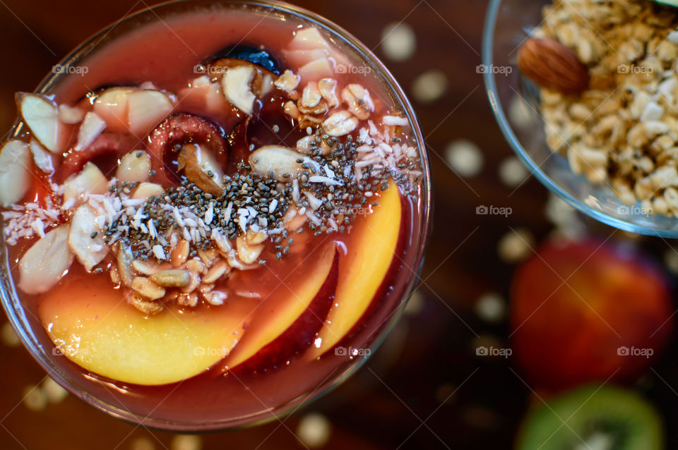 Smoothie bowls on table with granola muesli, almonds, fresh fruit and garnished with nectarine, black cherry, almond slice, sunflower seeds, coconut sprinkles, chia seed and fig healthy eating background photography