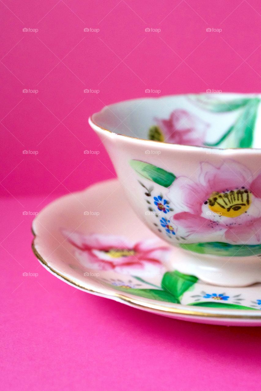 Closeup of an antique hand-painted floral teacup on a bright pink background 