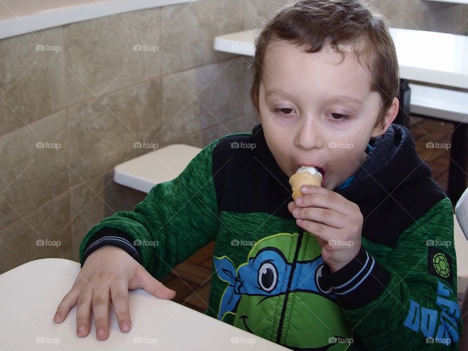 A little boy devours his vanilla ice cream cone. 