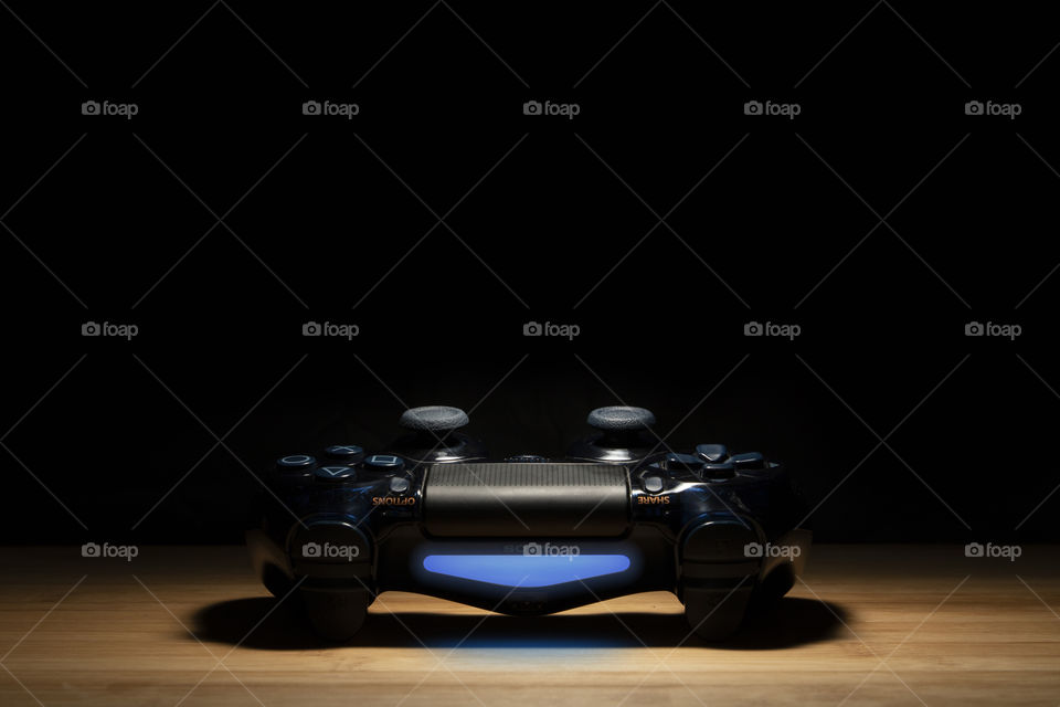A portrait of a turned on sony PlayStation 4 controller emerging from the dark like it is ikn a spotlight.