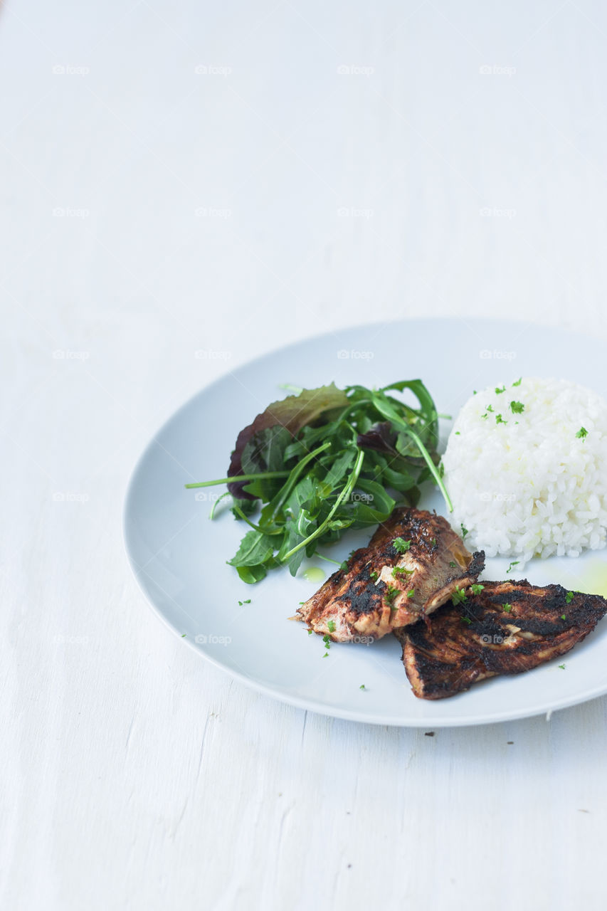 Food for a diet: grilled fish. White plate with grilled mackerel, rocket salad and boiled rice over white background. Dish for dieting. Healthy food.