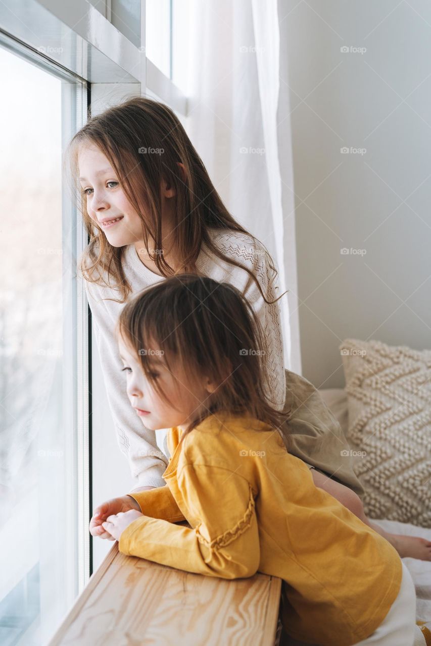 Cute little sisters girls looking in window at the home