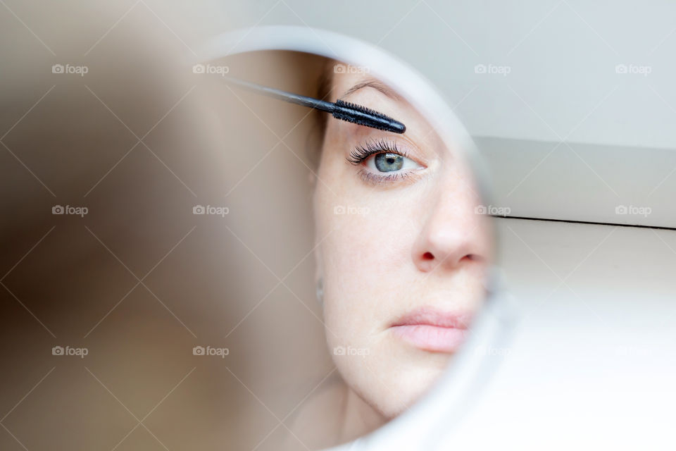 Woman applying mascara looking at the mirror