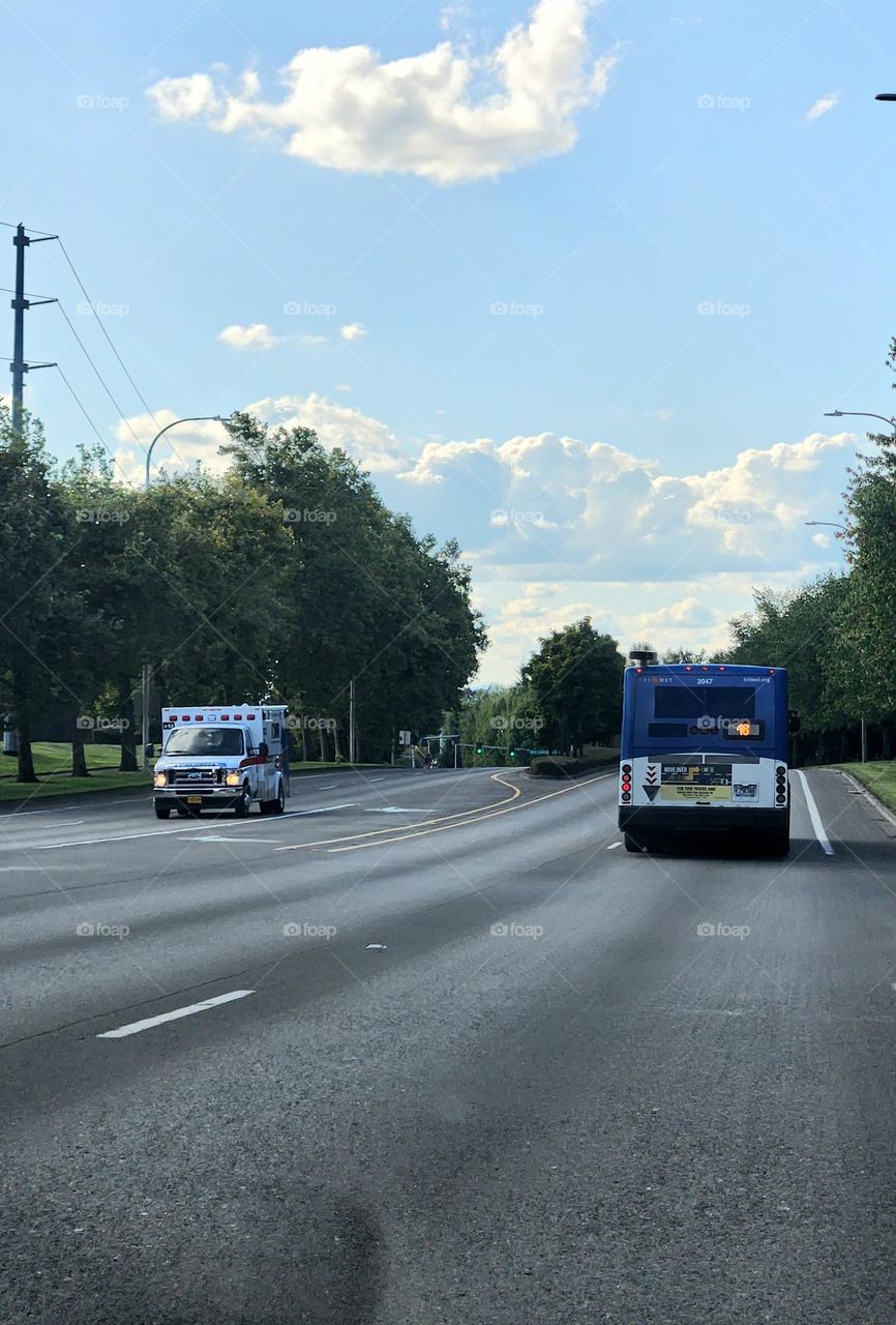 An ambulance passing a public bus in Oregon commuter traffic on a sunny Friday evening