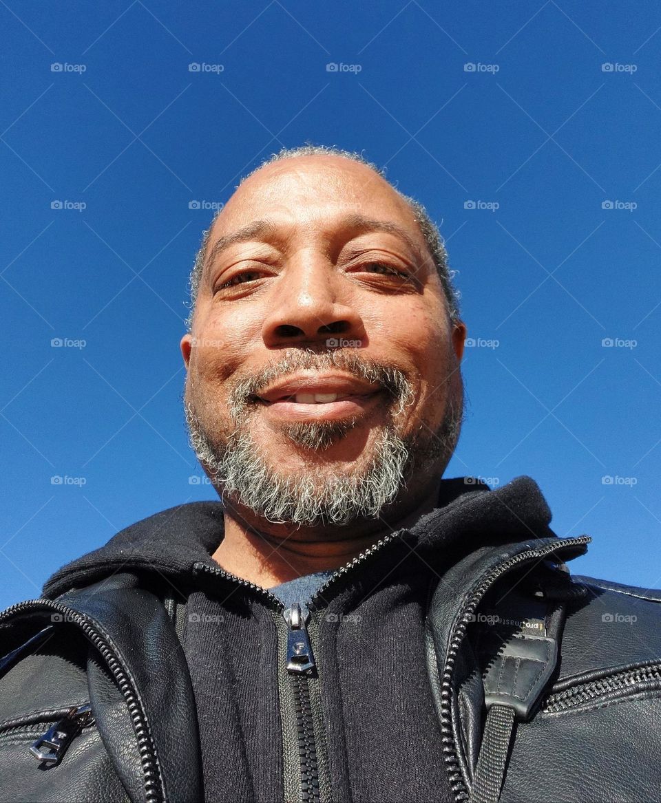 Self-portrait of a photographer along the riverfront with blue skies in the background