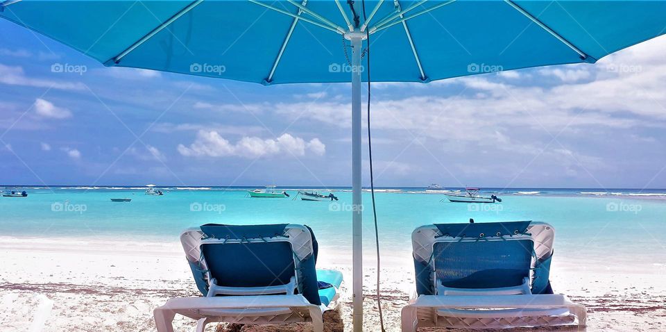 Bright blue Carribean sea with white beach and loungebeds undee blue umbrella