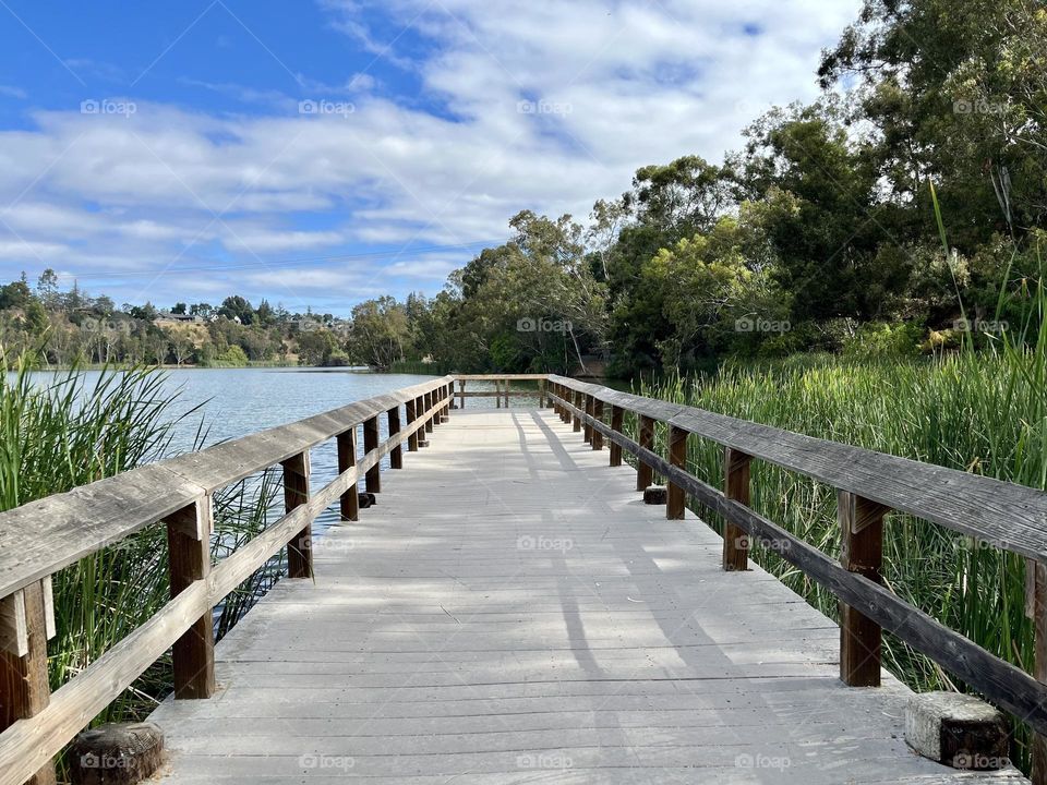 Follow to long, wooden path to the end of the pier on the lake under the blue cloudy skies