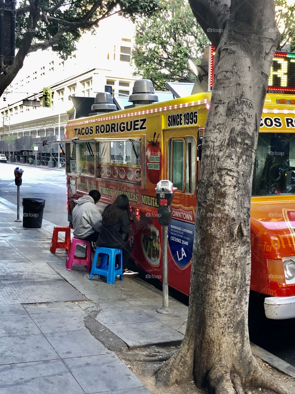 Brightly colored stools beckon patrons, as a young couple eats.  Taco truck in Downtown Los Angeles Ca 6.13.2020
