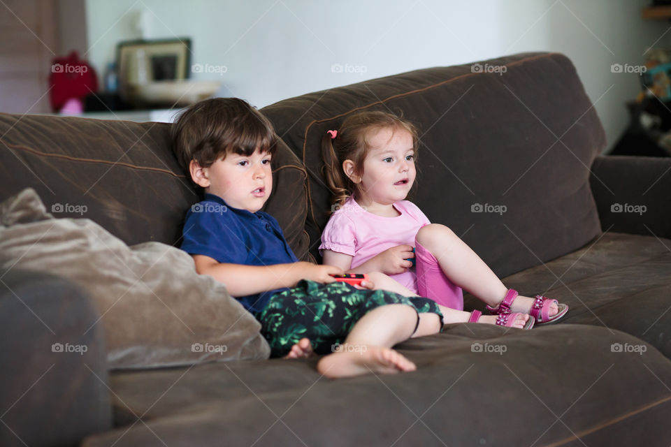 Concentrated toddlers boy and girl playing video game sitting on sofa at home