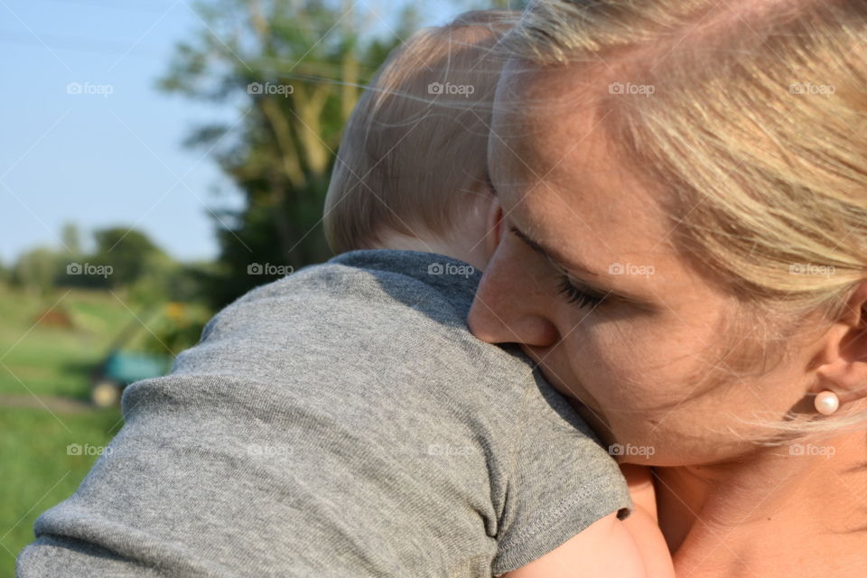 A close up of tender moment between mother and infant child, outdoors in the mild, late afternoon summer sun. 