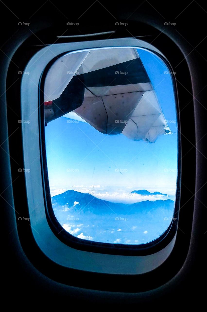 Flying above the clouds and mountains seen from behind the airplane window in eye level view