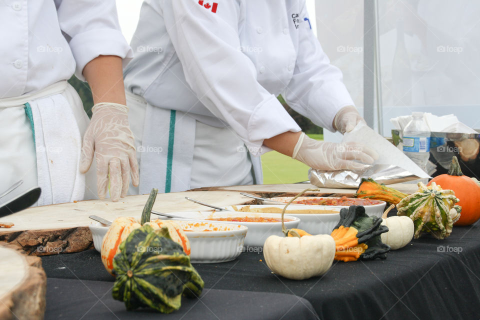 Two chefs in white uniforms prepare a delicious meal at an outdoor venue surrounded by fall harvest gourds 