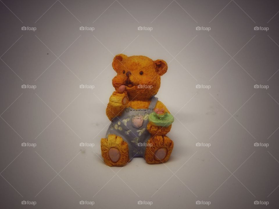 Small Tiny toy bear is sitting looking for something while eating.