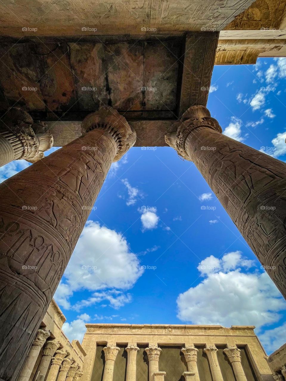 Clouds and blue sky seen from behind pillars at an ancient Egyptian temple with the temple in the background 