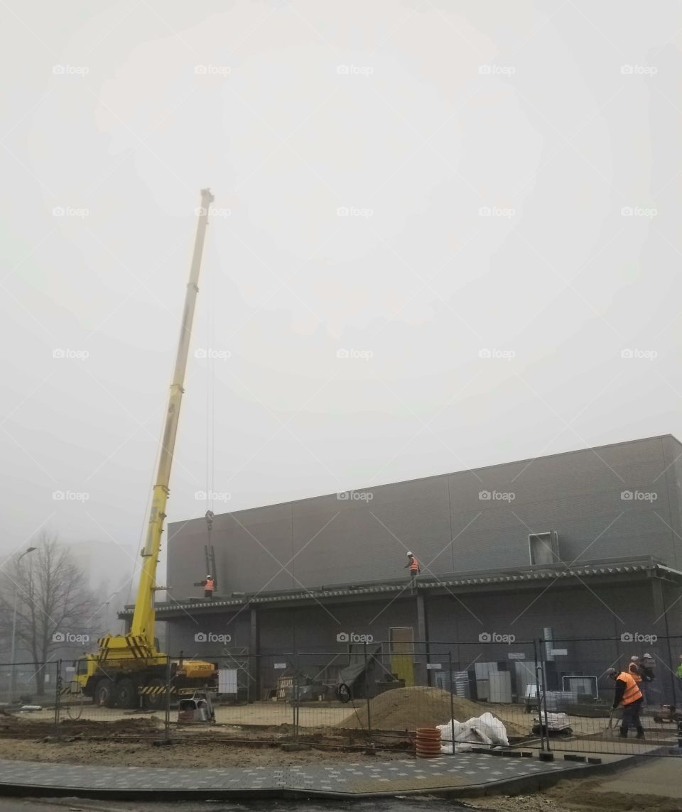 Building object with crane and working people in fog