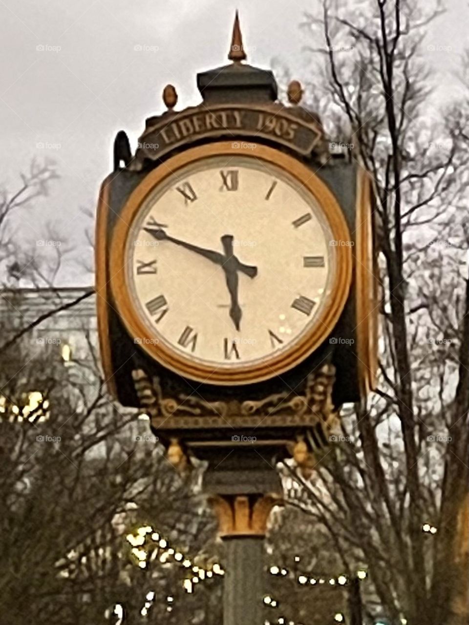 An antique clock from 1905, standing tall and proud in the heart of downtown Greenville, SC. The clock's intricate design features classic Roman numerals and ornate detailing on its metal frame.