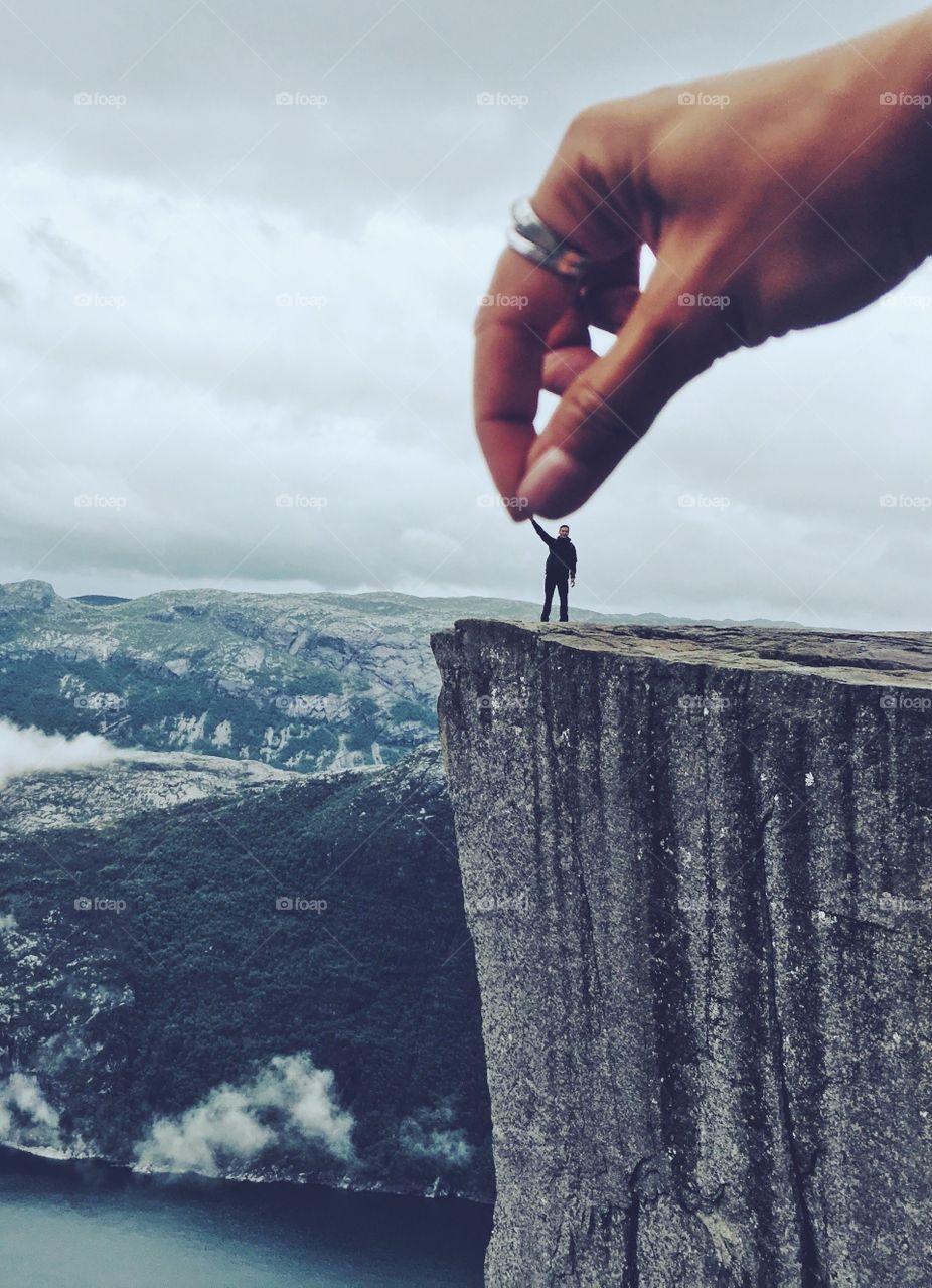 A huge hand is holding a tiny human on the top of the Prekestolen rock.