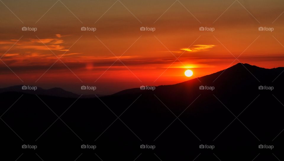 A bright red sunrise from the top of a high mountain. Another mountain is in shadow and creates a dramatic mood.