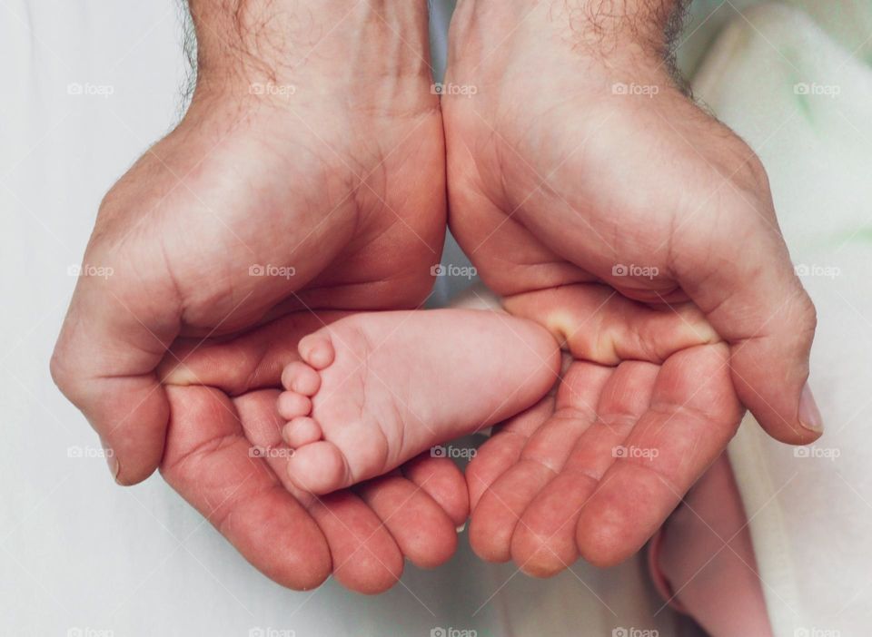 The hands of a caucasian male father hold in the palms of the foot of a newborn baby on a white background, top view close-up. The concept of newborns, baby body parts, dads.