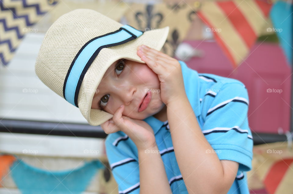 Young boy wearing a sun hat and making a goofy face in front of a colorful background outdoors