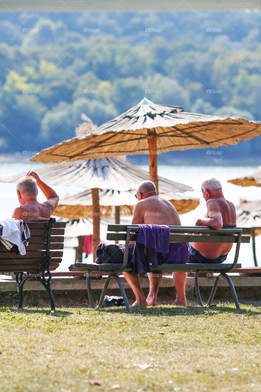 Three elder men sitting on the bench at the beach enjoying free time