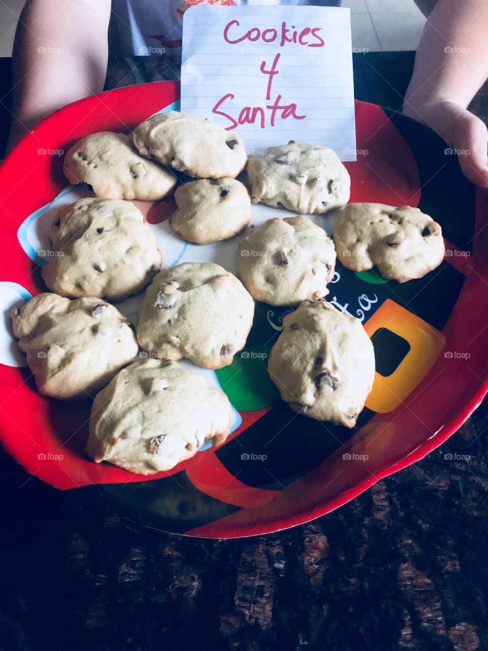 Cookies for Santa, A plate full of delicious chocolate chip cookies on a Christmas Santa Clause plate. Child holding a plate of Cookies for Santa.