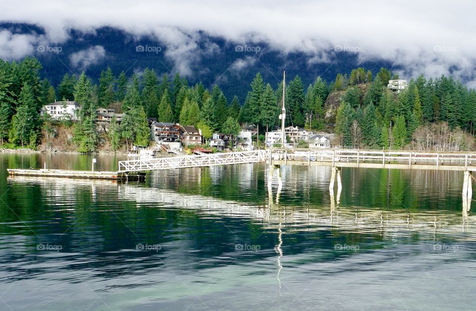 Dock across a glassy ocean bay in Belcarra British Columbia, calm mirror like water, large waterfront homes, landscape 