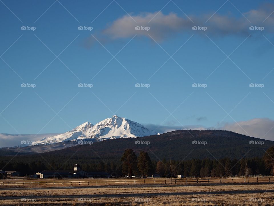 The majestic snow covered Three Sisters in Central Oregon’s Cascade Mountain Range overlook a farm field during the off-season on a beautiful sunny day. 