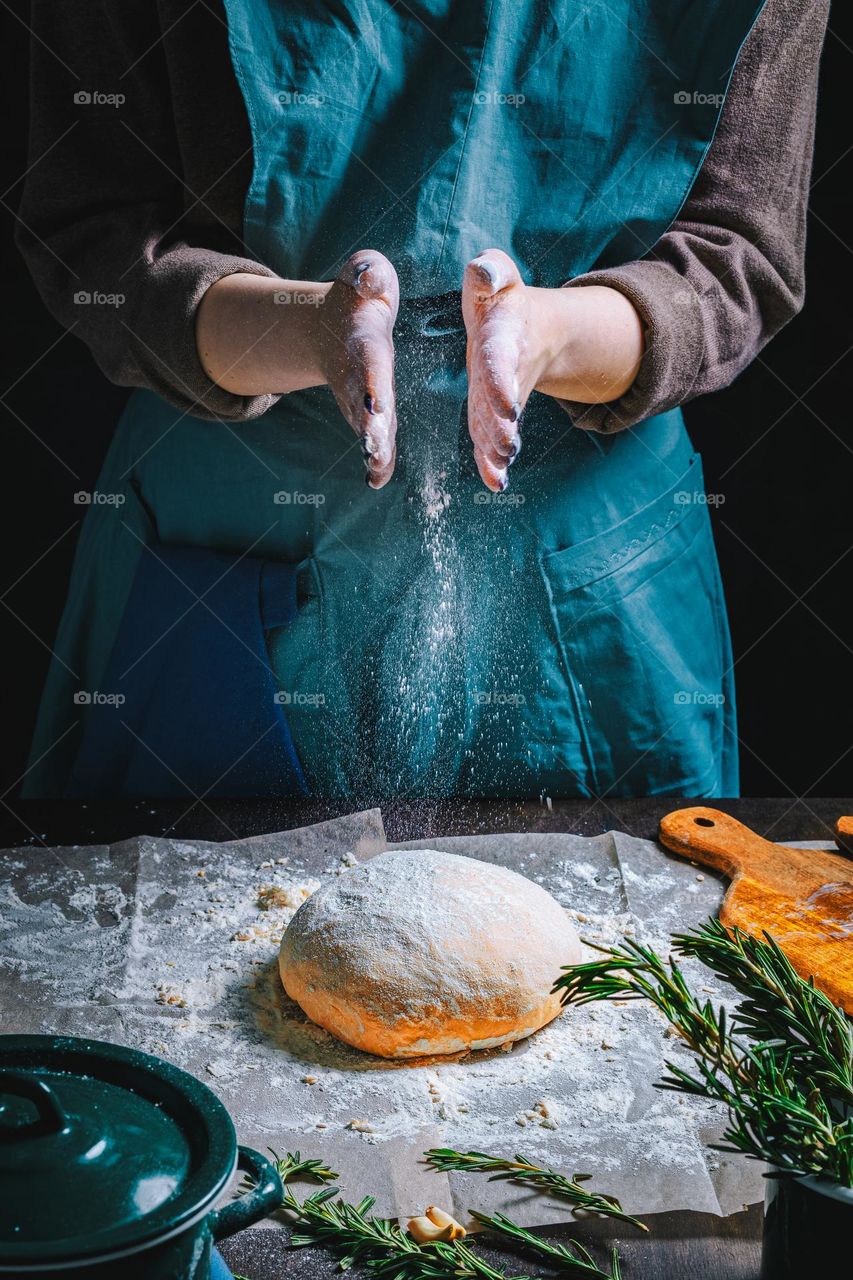 Women's hands, flour and dough. Levitation in a frame of dough and flour. A woman in an apron is preparing dough for home baking. Rustic style photo. Wooden table, wheat ears and flou.Emotional photo