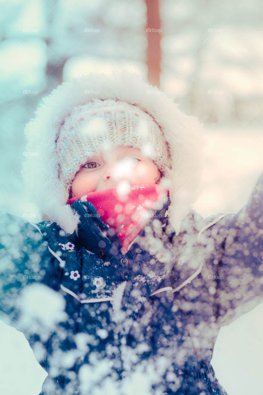 Happy smiling little girl enjoying snow. Toddler is playing outdoors in wintertime while snow falling. Toddler is wearing dark blue snowsuit and wool cap