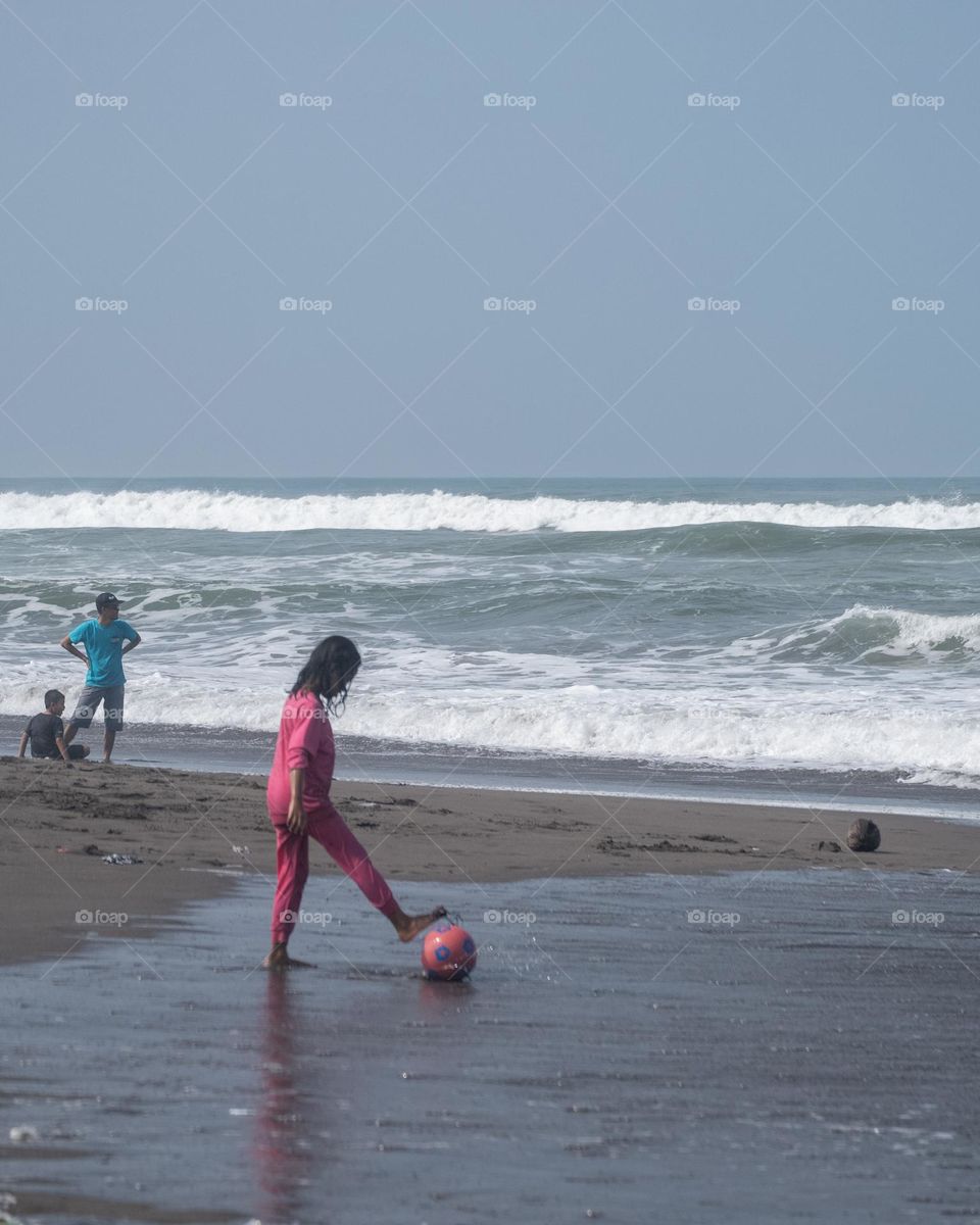 little girl playing football on the beach