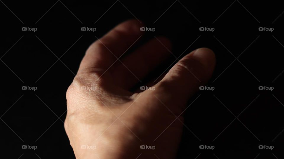 Partially lit Hand reaching out into striking darkness