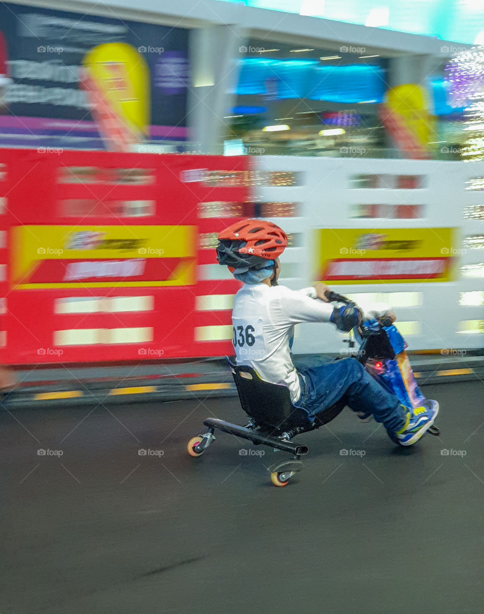 High-speed children's speedway competition on electric scooters. Racing, a boy in a helmet with a participant number quickly rides a three-wheeled scooter along the highway