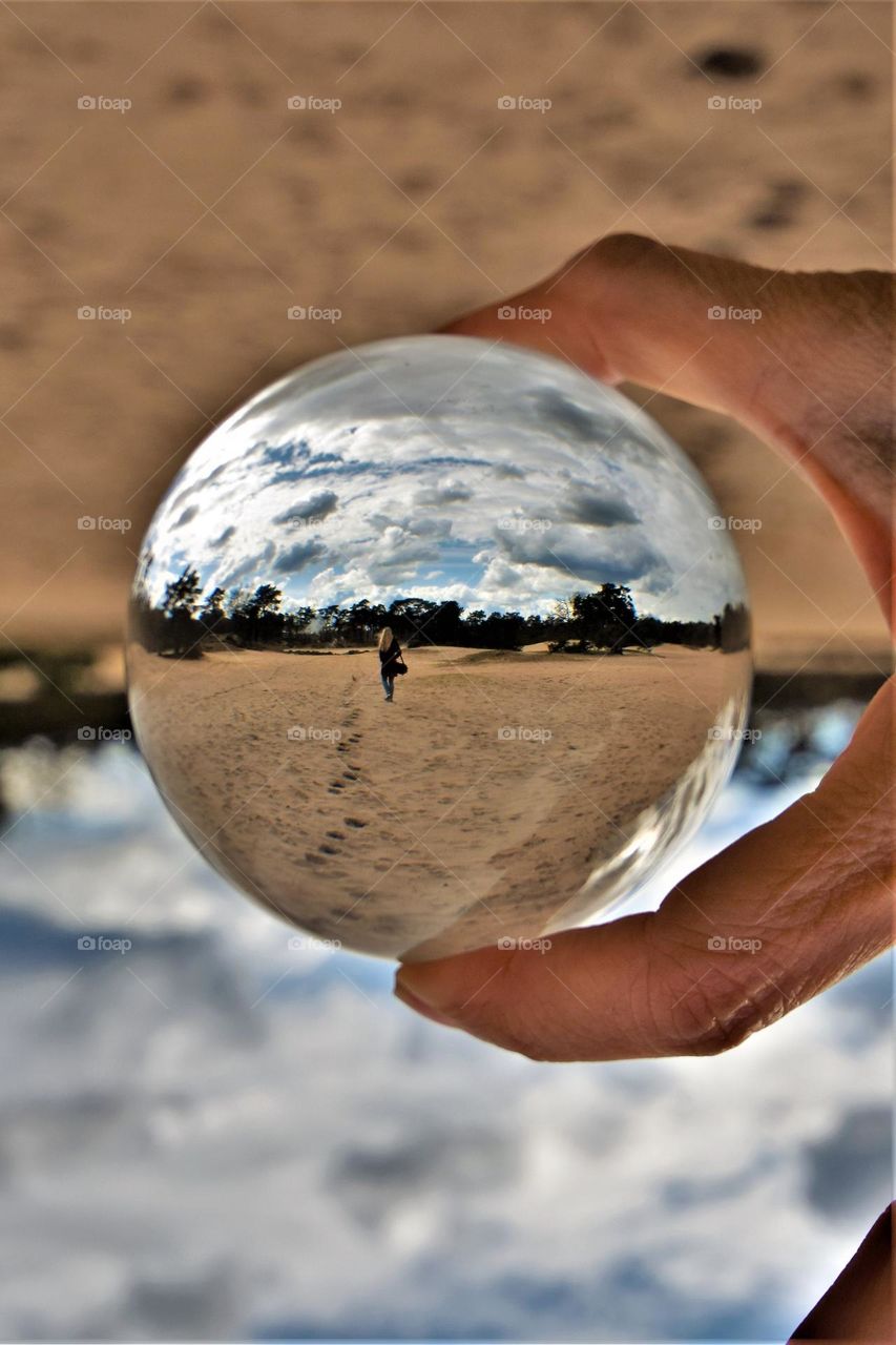 perspective wide angle image seen trough a clear glass ball with a woman walking away leaving her footprints in the sand