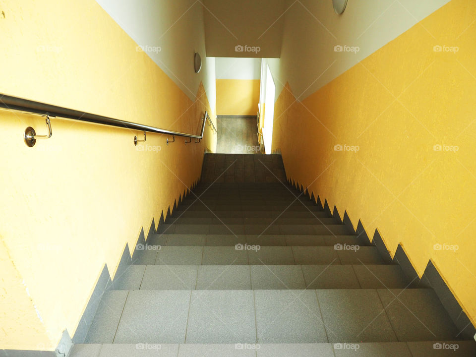 gray stairs descending down a yellow-and-white-walled corridor