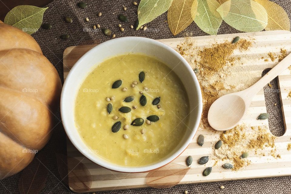 Spiced, cream of pumpkin soup viewed from above, with yellow & brown skeleton leaves