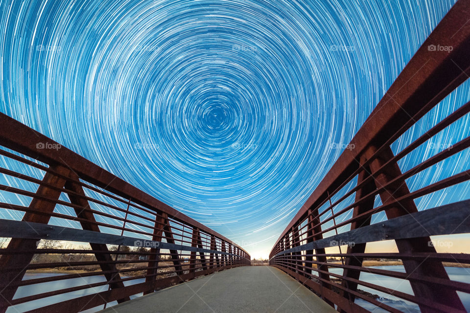 Leading lines of a wooden boardwalk facing north at the circular star trails around Polaris, as the Earth spins on its axis. 