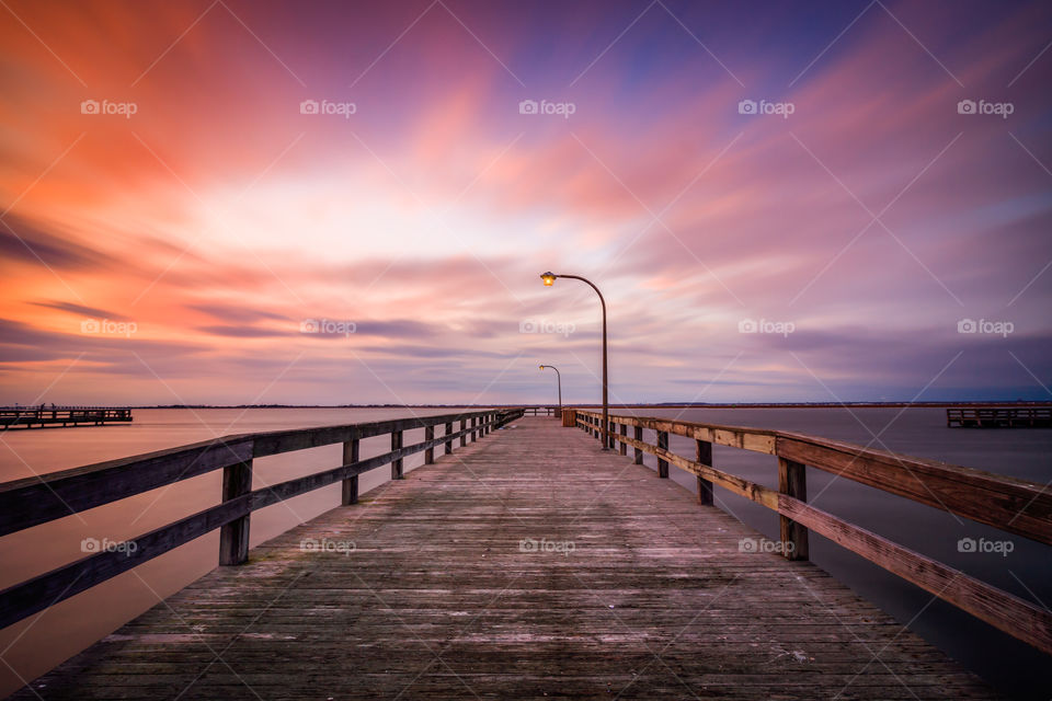 Old wooden pier leading into the ocean at sunset.