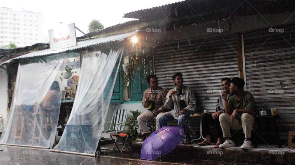 Semarang, Central Java, Indonesia - December 5, 2023: A group of teenagers are cooling off during the rain by joking around and enjoying coffee at a hangout place in Semarang, Indonesia