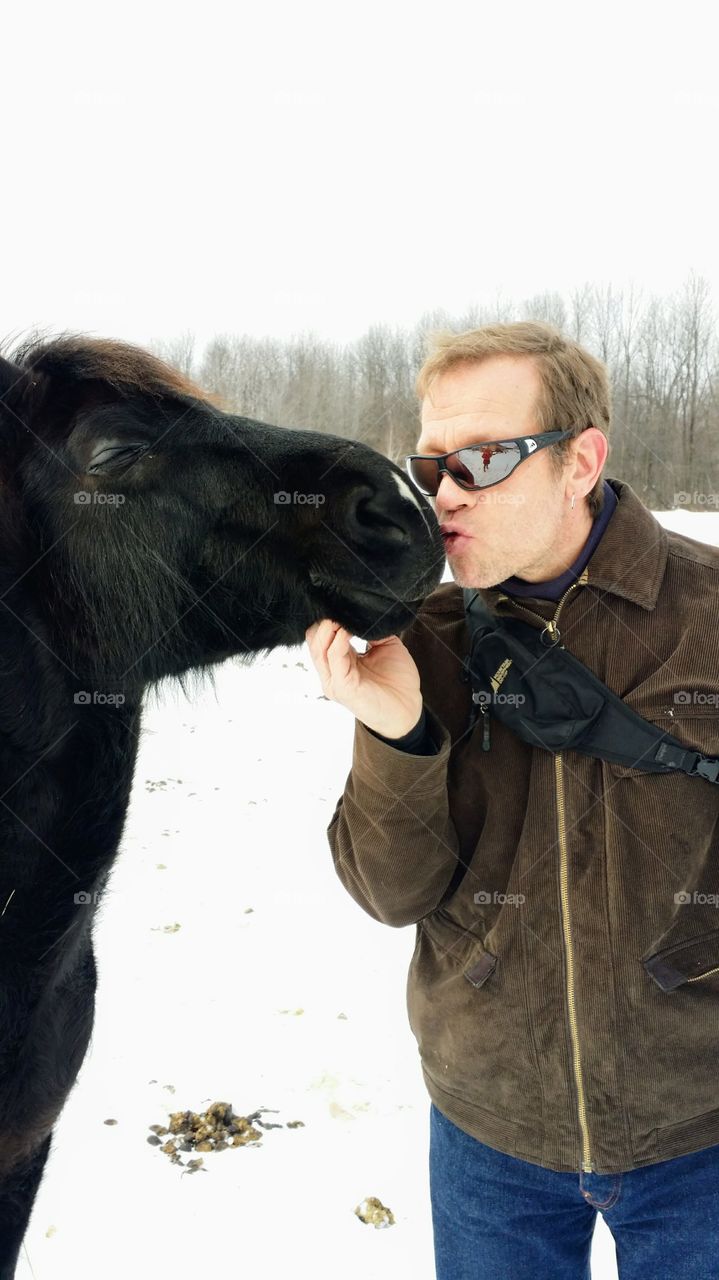 Close up of a man giving a kiss to a black horse standing in the snow