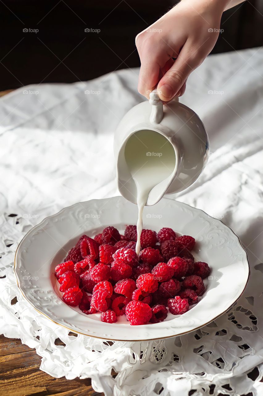 Close up milk being poured into a plate full of bright red raspberries.