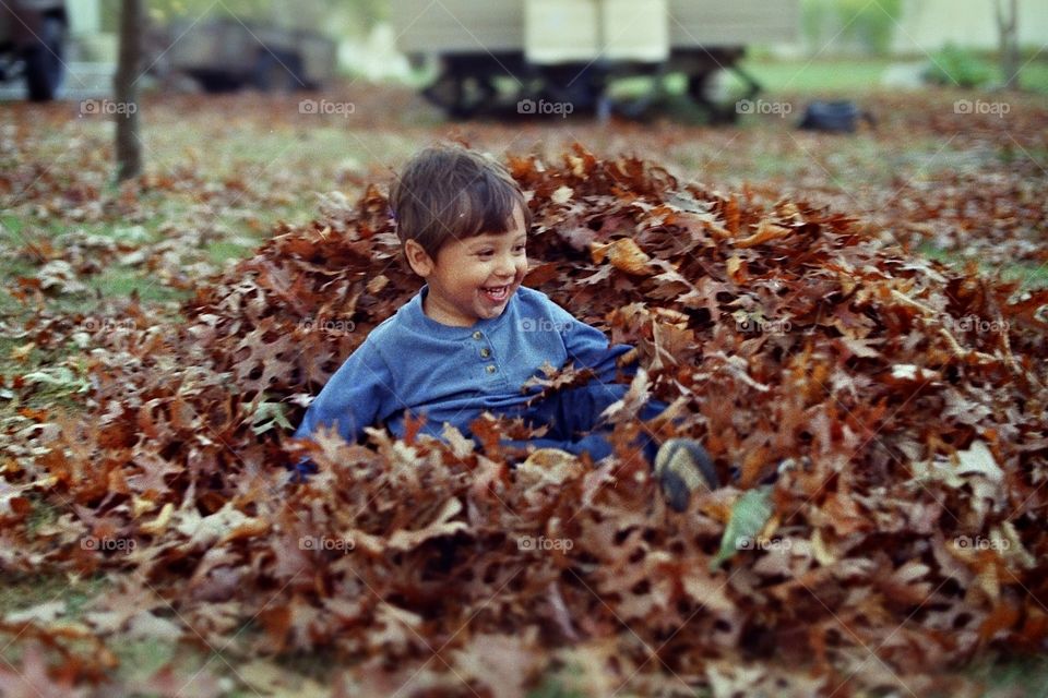 Happy boy sitting in dry autumn leaves